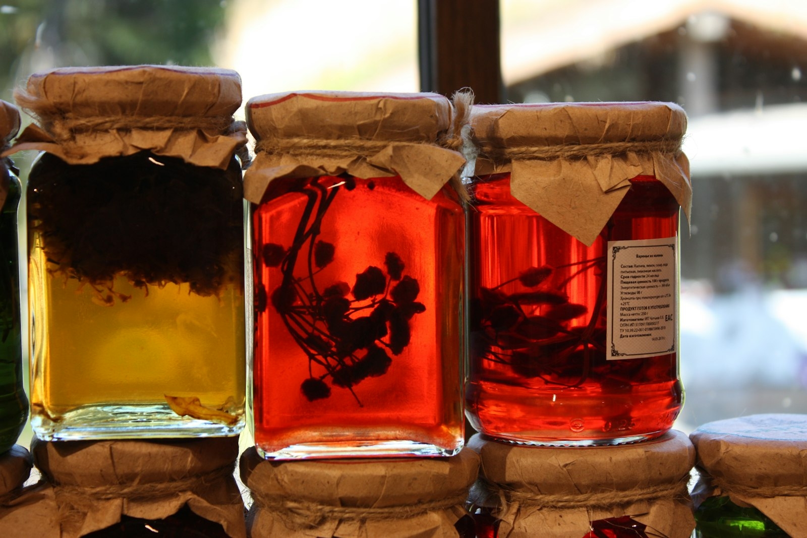 Jars of homemade preserves with paper-and-twine lids, backlit by warm daylight.